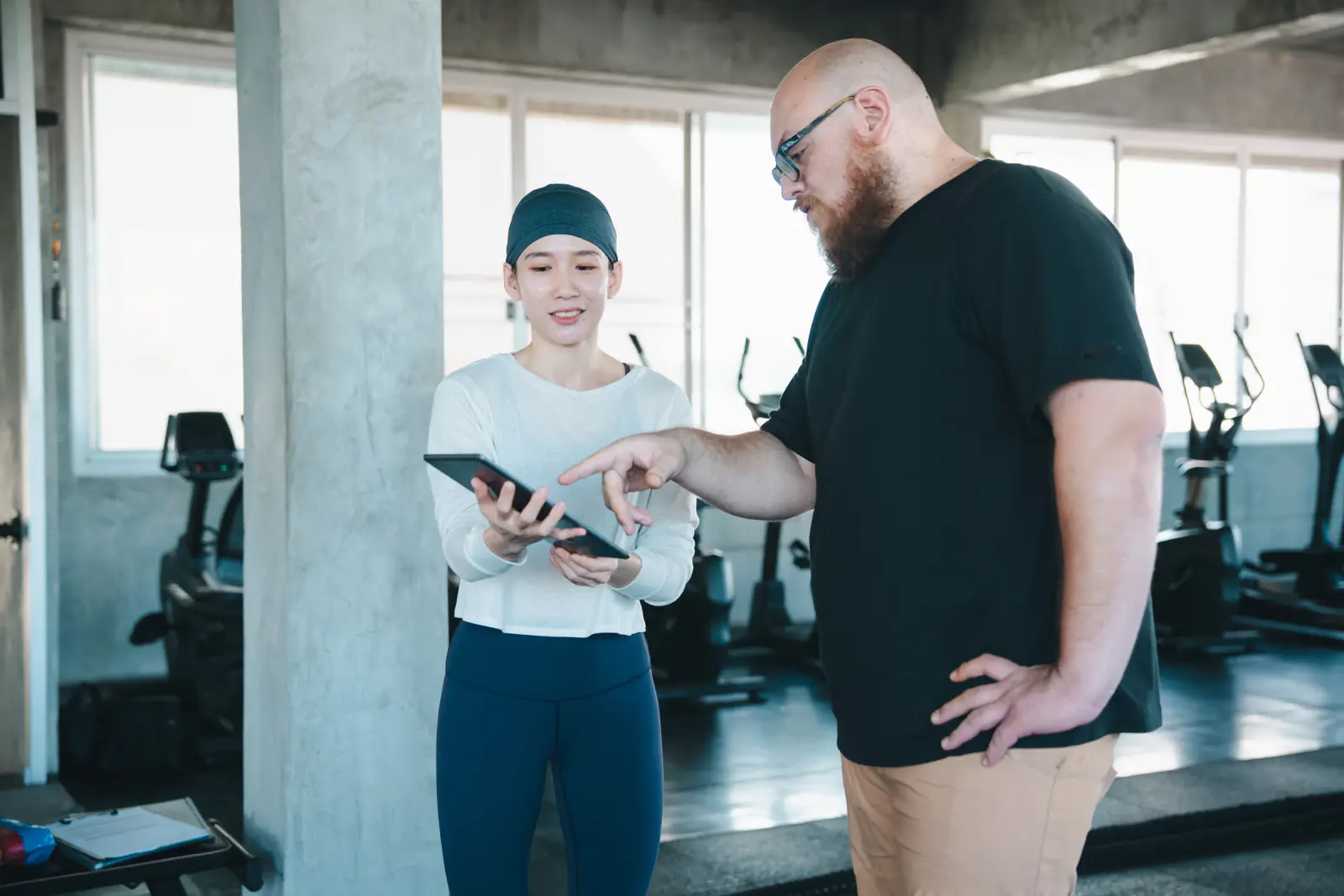 Two people look at a tablet in a gym.