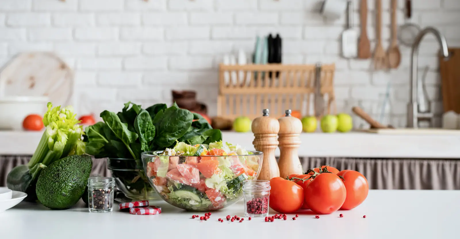 A bowl of salad, leafy greens, tomatoes and an avocado on a white kitchen counter.